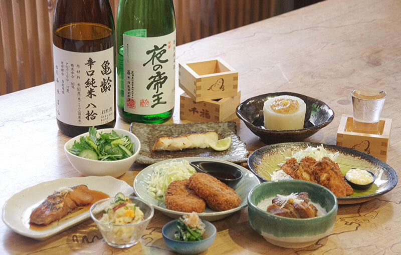 広島の地酒と居酒屋の小皿料理が並ぶ木のテーブル。
